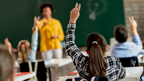 A child raises her hand in a classroom. 