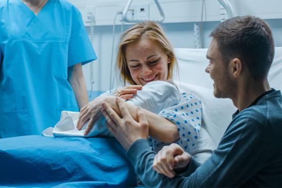 A mother and father are seen with their newborn baby in a hospital room