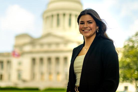 Amelia Ford stands smiling in front of the Arkansas State Capitol