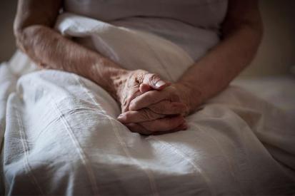 An elderly woman is seen in bed with her hands folded over her lap