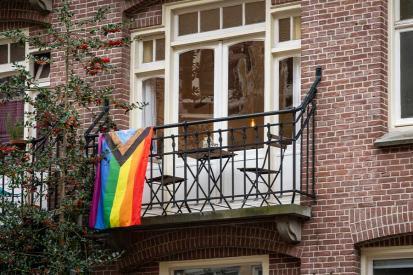 A Pride flag hangs on the balcony of a brick building