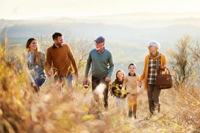 A family with children, parents, and grandparents is seen walking up a hill for a picnic