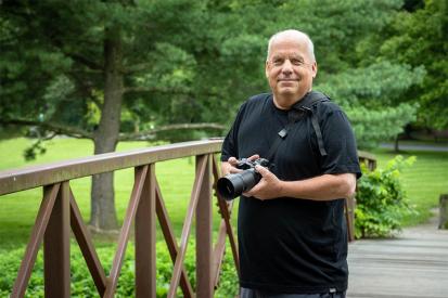 Photographer Bob Updegrove is seen standing on a park bridge with his camera