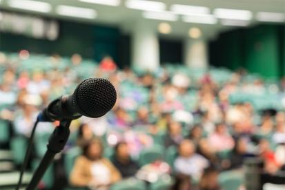 A microphone is set up in front of an audience in stadium-style seats