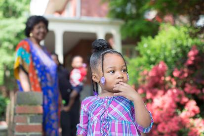 A foster child in a purple dress stands outside a brick house