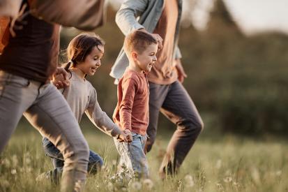 A mom and dad and their two kids run through a sunny field