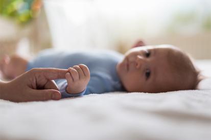 A baby boy holds his parent's finger