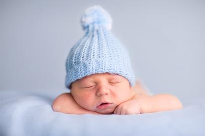 A baby wearing a blue beanie sleeps on a blanket