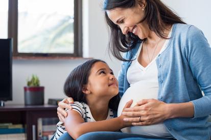 A pregnant mother and her daughter smile at each other