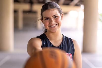 Amelia Ford smiles as she holds a basketball out toward the camera