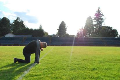 Coach Joe Kennedy kneels on the football field at Bremerton High School in Washington