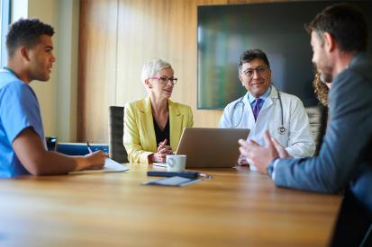 A group of doctors and other health-care professionals sit around a table