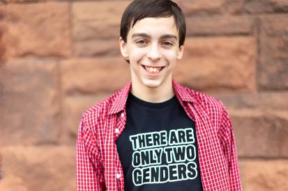 Liam Morrison wearing his "There are only two genders" shirt in front of a brick wall