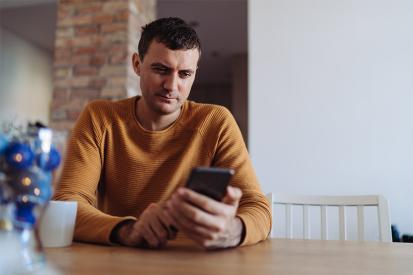 A man sits at a table reading from his mobile phone