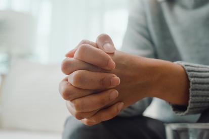 A person sits with their hands clasped