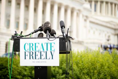 Microphones sit on a podium with a sign that reads 'Create Freely' in front of the U.S. Capitol