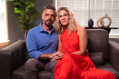 Dan and Jennifer Mead sit on a leather couch looking into the camera