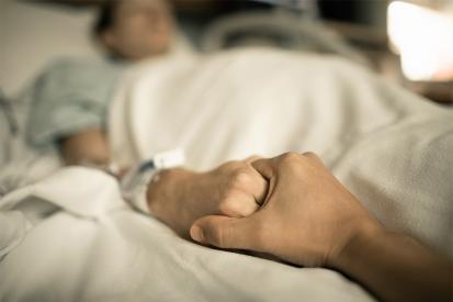 A woman in a hospital bed holds a man's hand