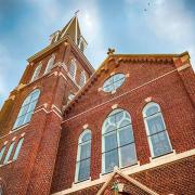 A brick church is seen on a bright sunny day with clouds behind the steeple