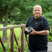 Photographer Bob Updegrove is seen standing on a park bridge with his camera