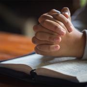 Folded hands praying over the bible