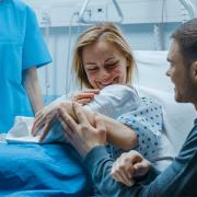 A mother and father are seen with their newborn baby in a hospital room