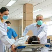 Medical professionals in a hospital wheel a patient down a hallway in a stretcher