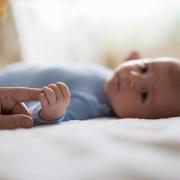 A baby boy holds his parent's finger