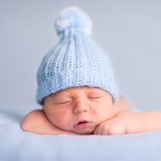 A baby wearing a blue beanie sleeps on a blanket