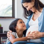 A pregnant mother and her daughter smile at each other