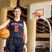 Amelia Ford holds a basketball on the court with a hoop in the background