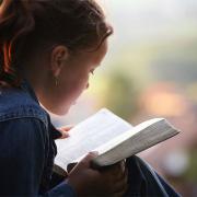 Girl in a jean jacket reading the Bible