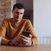 A man sits at a table reading from his mobile phone