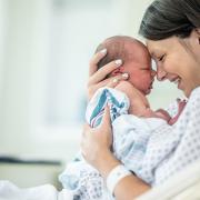 A mother smiles and holds her newborn baby