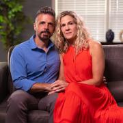 Dan and Jennifer Mead sit on a leather couch looking into the camera