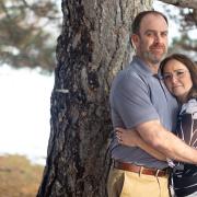 Joe and Serena Wailes hugging and standing by a tree