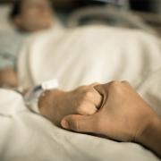 A woman in a hospital bed holds a man's hand