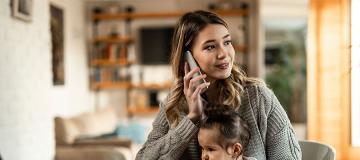 A young mother talks on the phone while her child in her lap