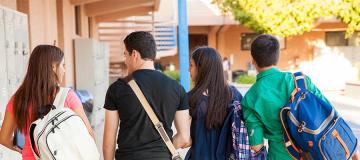 A group of teenage students walk across campus to class