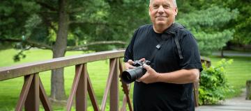 Photographer Bob Updegrove is seen standing on a park bridge with his camera