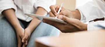 A doctor takes notes as he meets with an adolescent patient