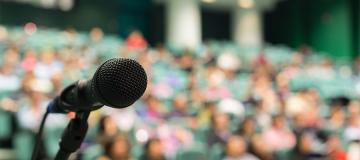 A microphone is set up in front of an audience in stadium-style seats