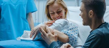 A mother and father are seen with their newborn baby in a hospital room