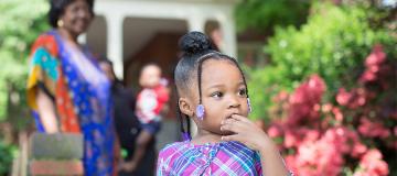 A foster child in a purple dress stands outside a brick house