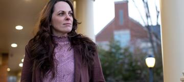 Elizabeth Gillette stands on a porch looking into the distance on a cloudy day