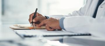 A doctor wearing a lab coat writes notes