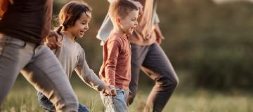 A mom and dad and their two kids run through a sunny field