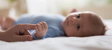 A baby boy holds his parent's finger