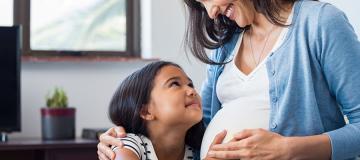 A pregnant mother and her daughter smile at each other