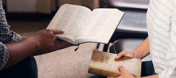 Two people study the Bible together in a classroom